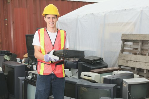 Operative wearing PPE loading rubbish into a skip with machinery nearby