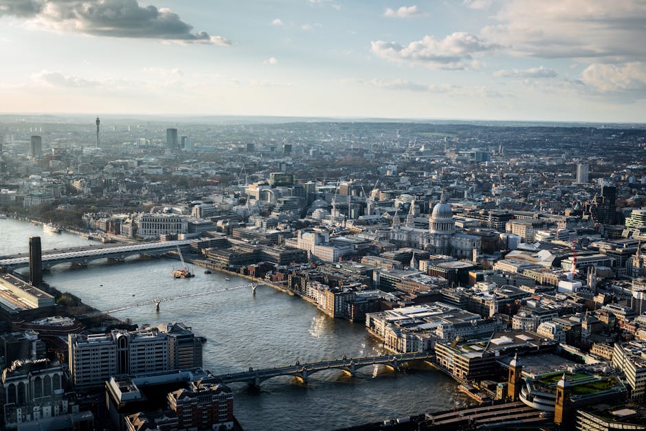 An aerial view of central London showing the River Thames flowing through the city with several bridges crossing over it. Prominent in the foreground are a mixture of modern and historic buildings, in